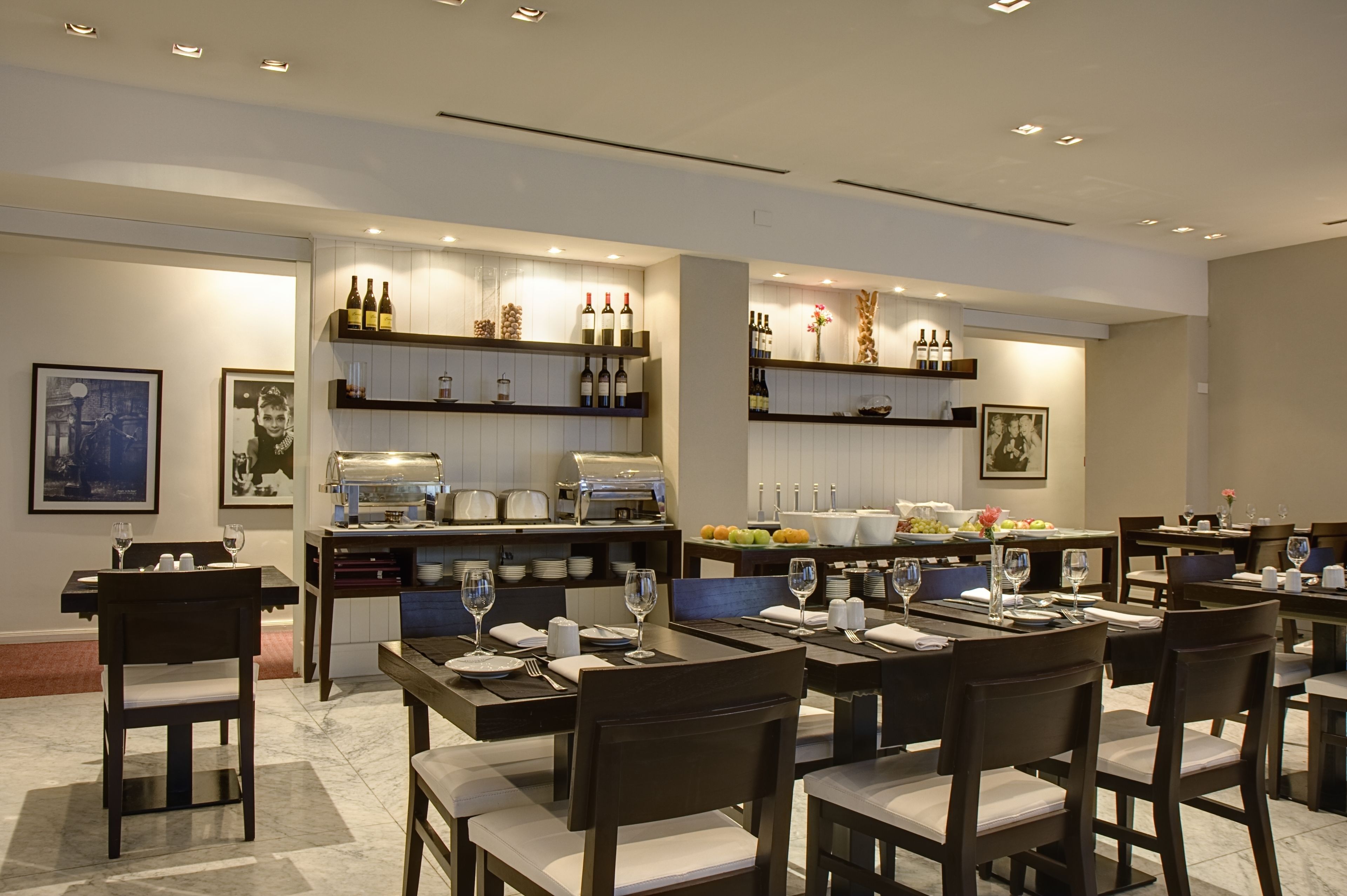 A modern dining area with multiple tables and chairs, a bar area with wine bottles, and a buffet setup.