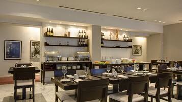 A modern dining area with multiple tables and chairs, a bar area with wine bottles, and a buffet setup.