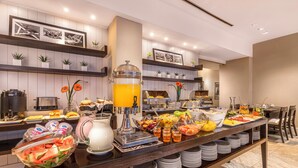 Una mesa de buffet con diversos alimentos, un dispensador de jugo y múltiples recipientes.