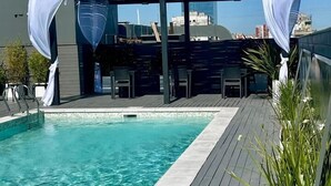 Una piscina en la azotea con cubierta de madera, cortinas blancas y vistas a la ciudad.