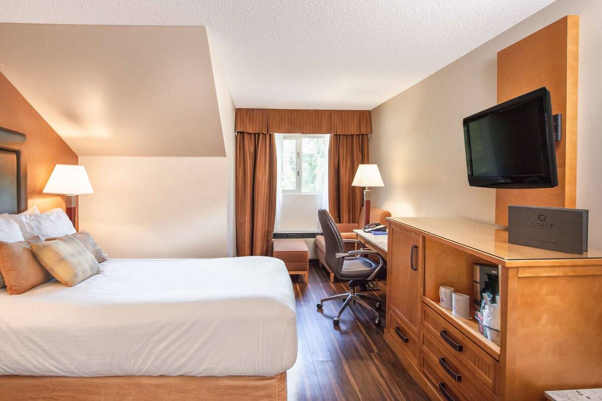 A hotel room with a bed, desk, chair, TV, and a window with curtains.