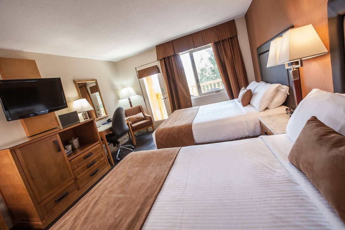 A hotel room with two beds, a TV, a desk, and a window with curtains.