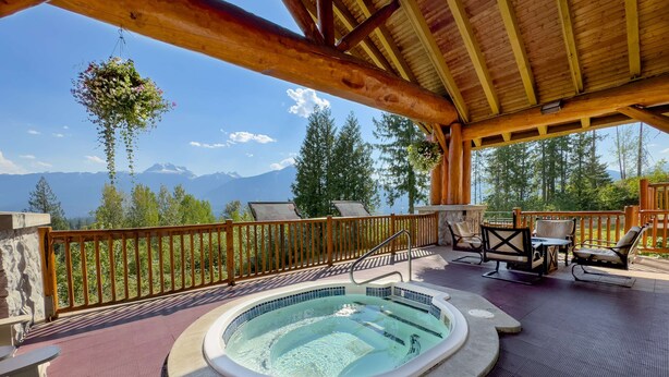 A wooden deck with a hot tub, outdoor seating, and a view of mountains.