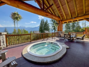 A wooden deck with a hot tub, outdoor seating, and a view of mountains. - Coast Hillcrest Hotel (Revelstoke)