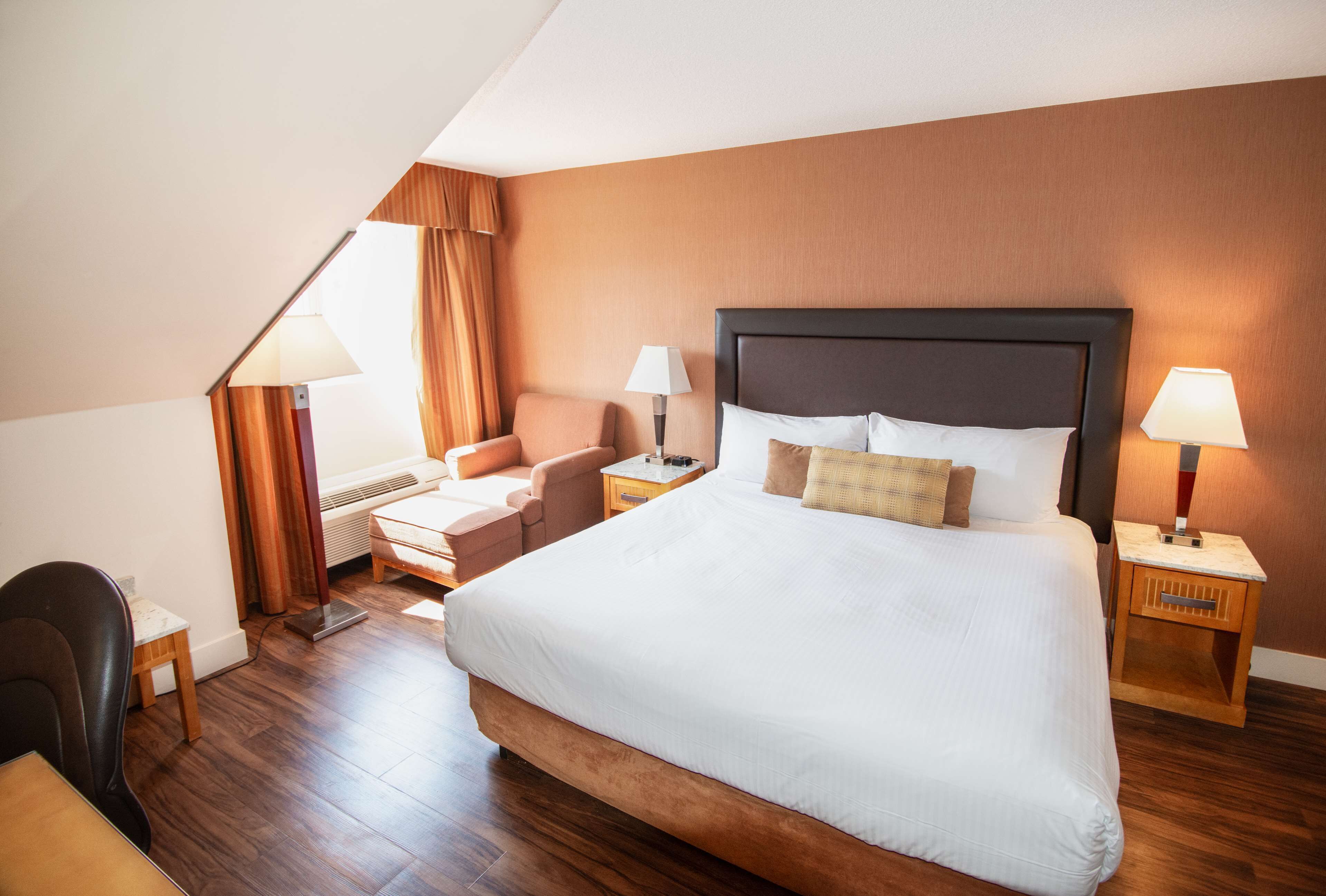 A hotel room with a large bed, two bedside tables, a chair, a desk, and a window with curtains.