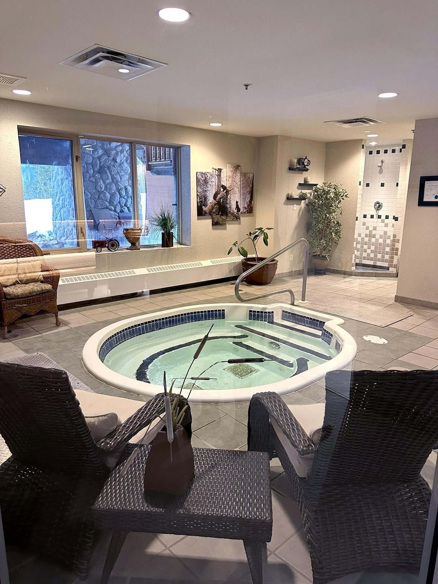 Uma área de spa com hidromassagem, cadeiras de vime, uma janela com vista e uma parede com chuveiro revestido em azulejos.