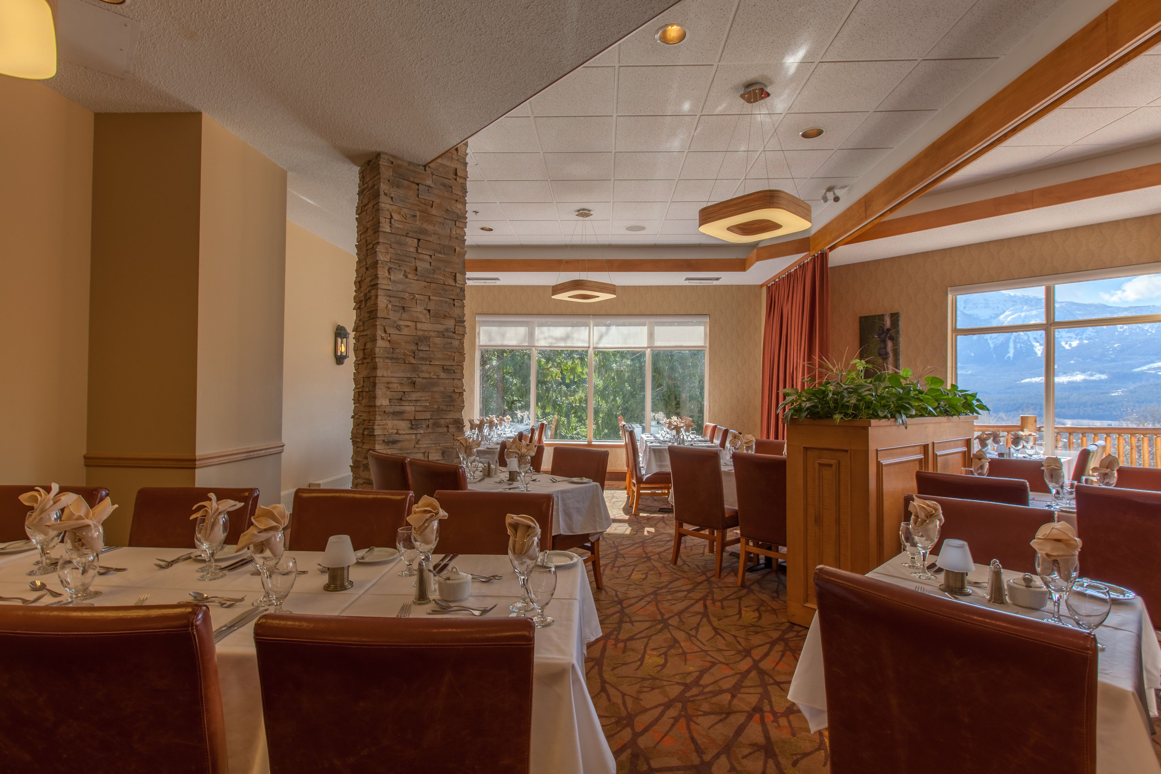 A dining area with tables set for service, a stone pillar, and a view of the outdoors.