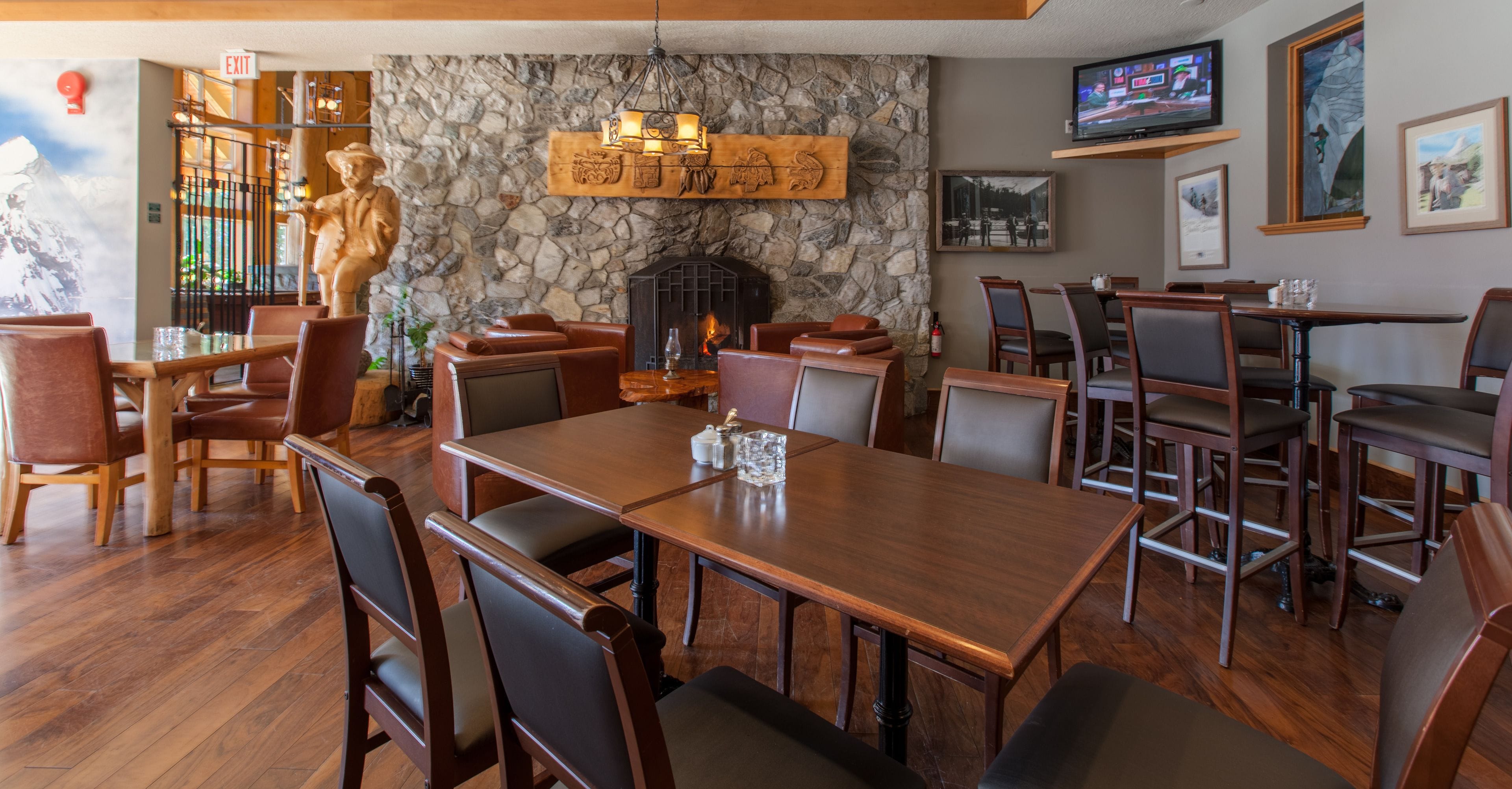 Un restaurante con pared de piedra, muebles de madera, chimenea y televisor montado en la pared.