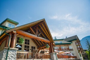 A multi-story building with a wooden facade, stone foundation, and balconies with umbrellas.