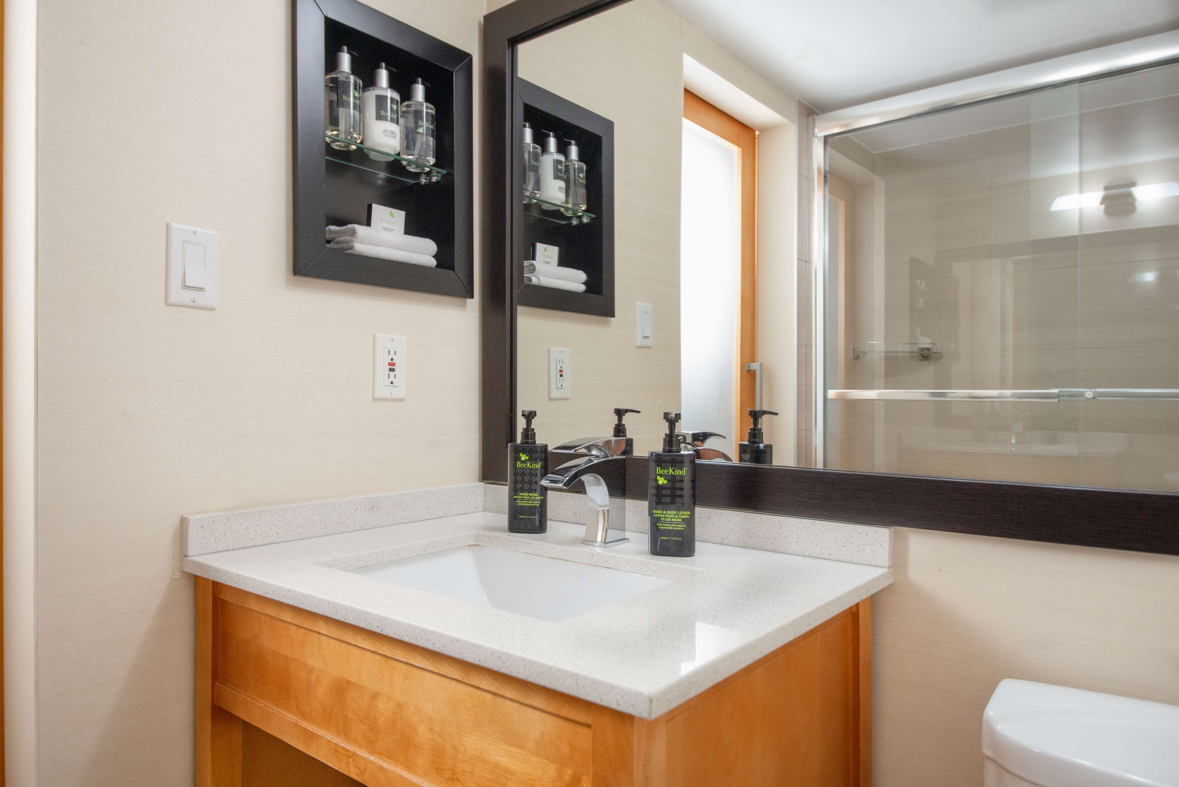 A bathroom with a white sink, wooden vanity, two mirrors, and a glass shower enclosure.