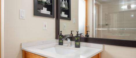 A bathroom with a white sink, wooden vanity, two mirrors, and a glass shower enclosure.