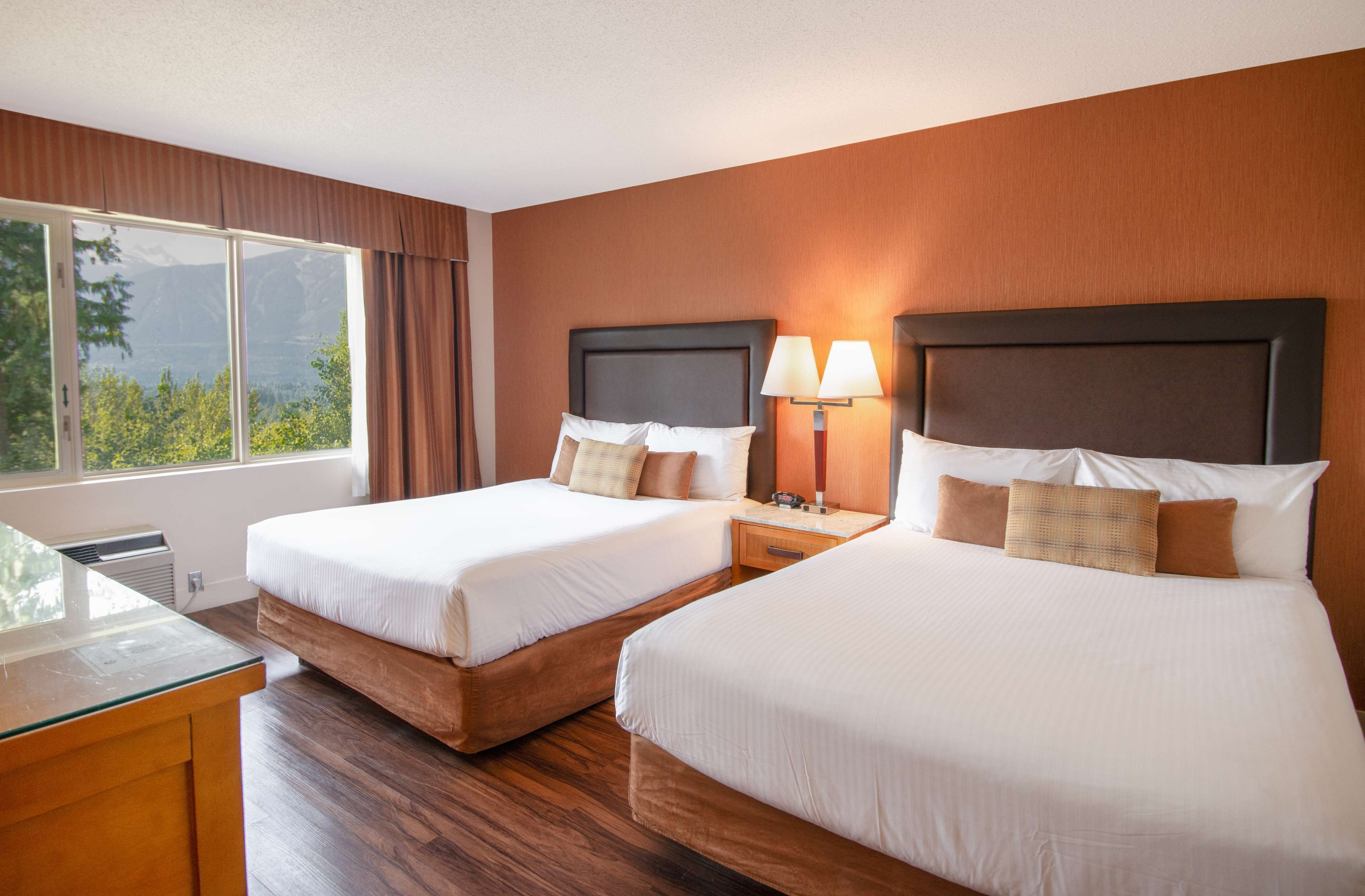 Habitación de hotel con dos camas, un escritorio y una ventana con vista a la montaña.