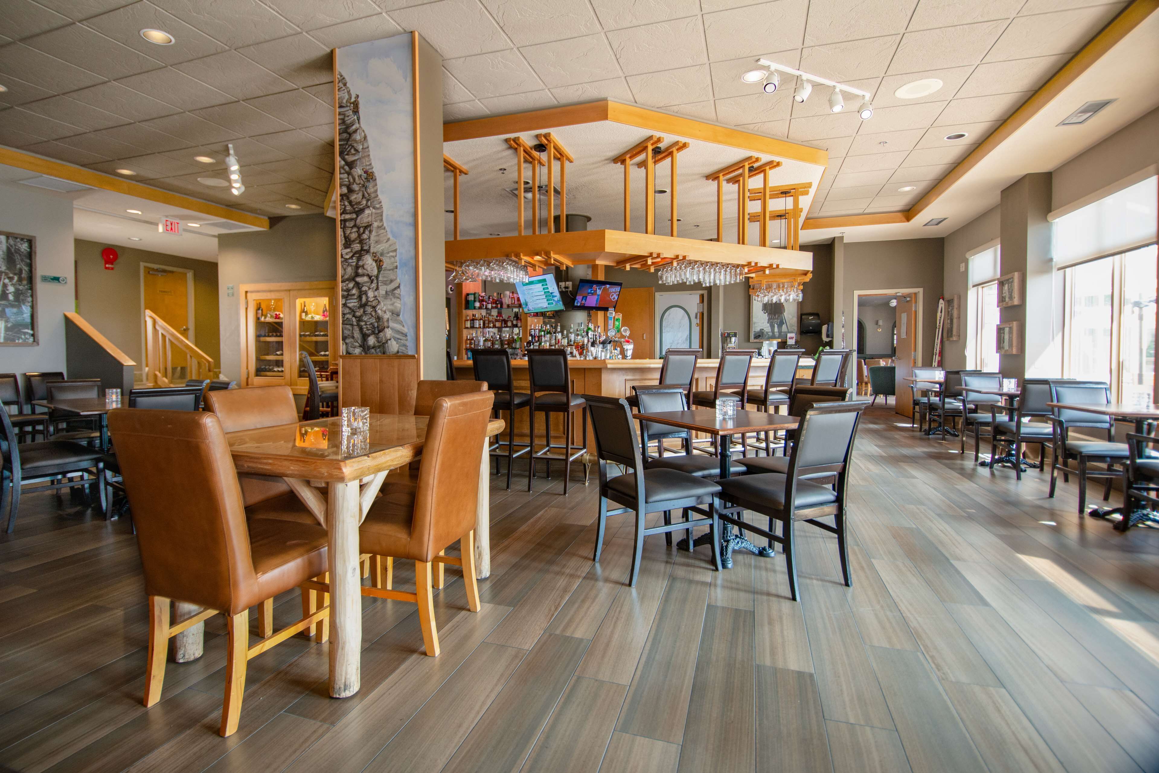 Un restaurant spacieux avec des tables et des chaises en bois, un coin bar et de grandes fenêtres laissant entrer la lumière naturelle.
