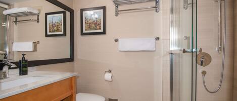 A modern bathroom with a glass shower enclosure, a white toilet, a sink with a mirror, and two framed floral paintings on the wall.