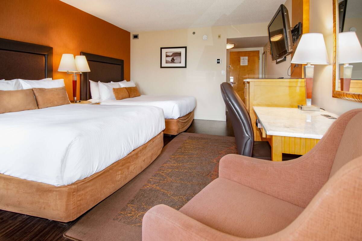 A hotel room with a double bed, a desk, a chair, a television, and a mirror.