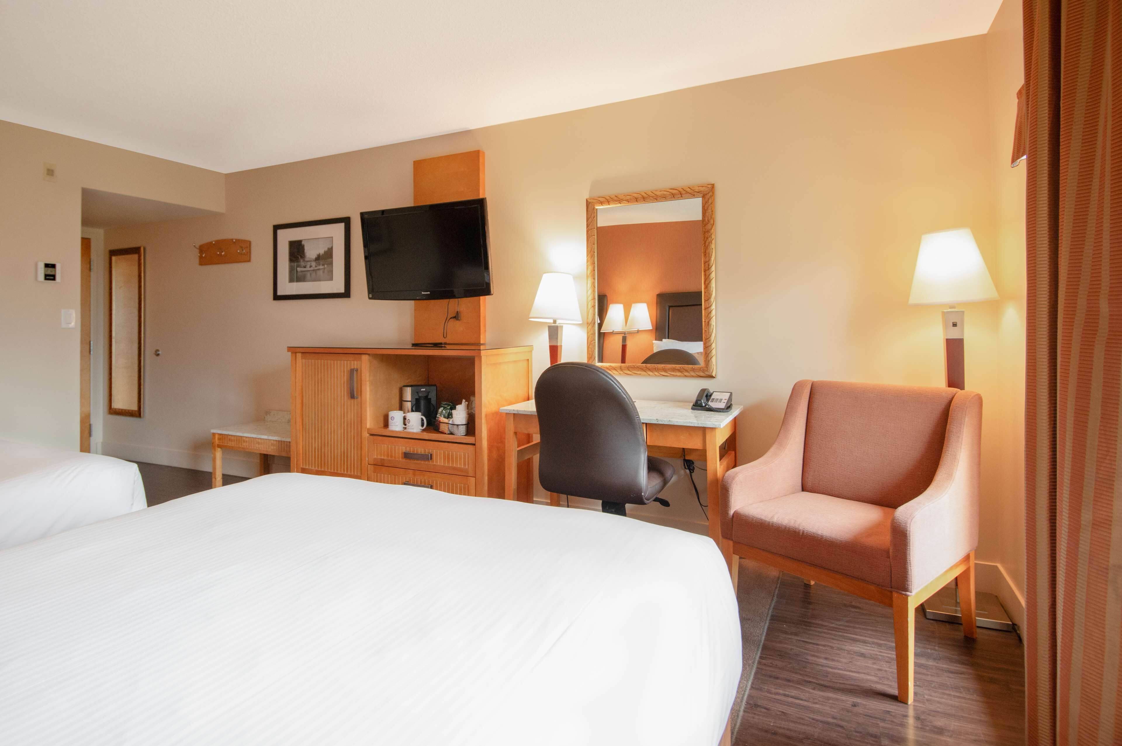 Ett hotellrum med två sängar, ett skrivbord med en stol, en tv, en spegel och två lampor.