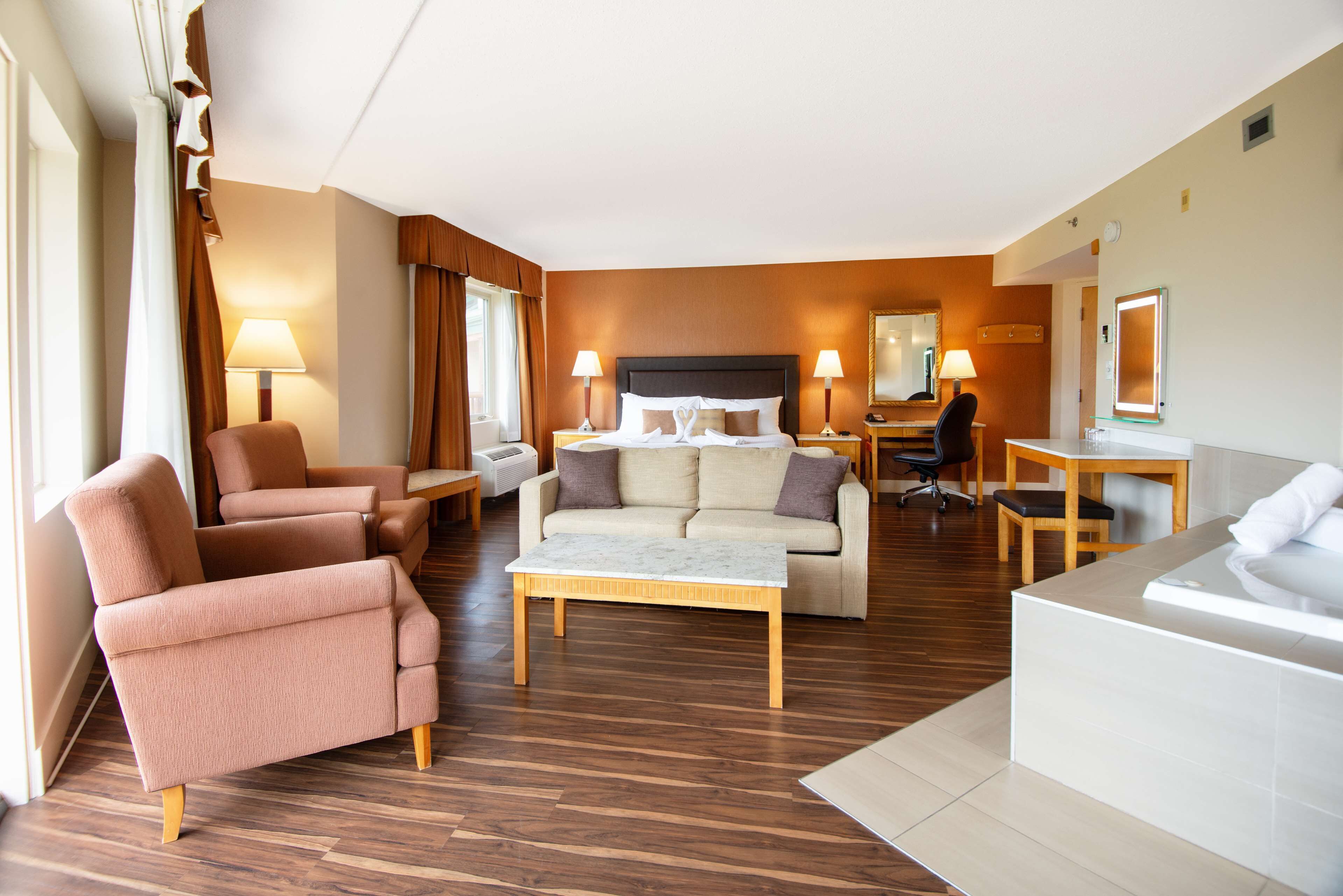 A hotel room with a bed, two armchairs, a sofa, a desk, and a bathroom.