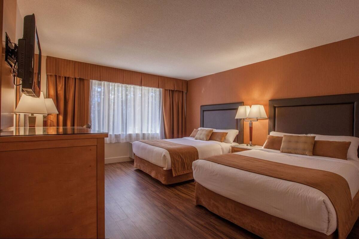 A hotel room with two beds, a desk, a TV, and a window with curtains.