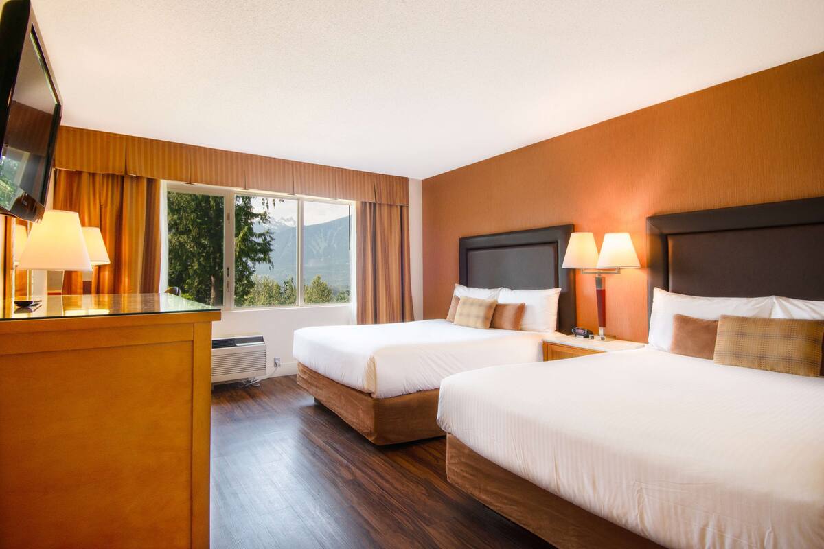 A hotel room with two beds, a TV, a desk, and a window with curtains.