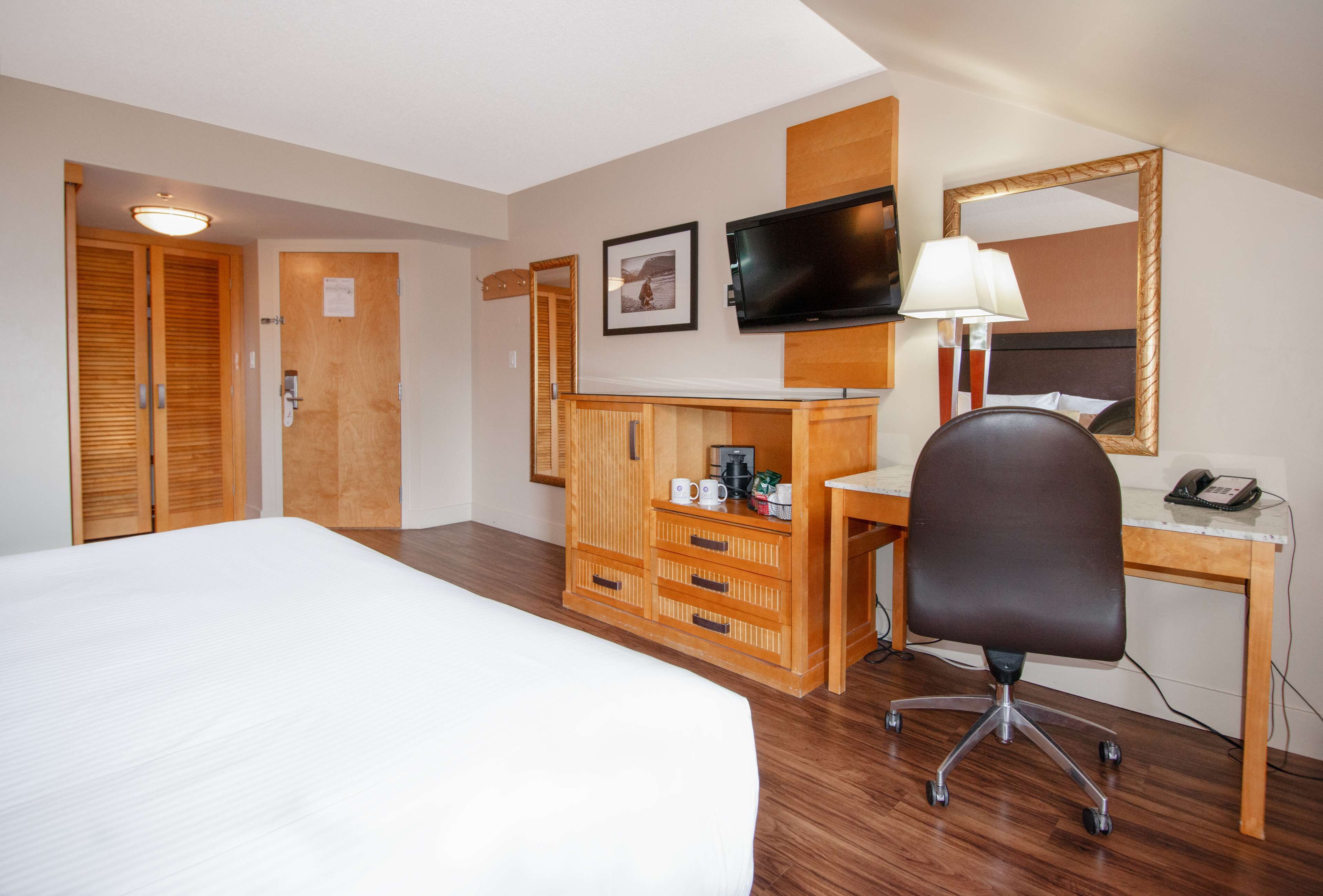 A hotel room with a bed, wooden wardrobe, desk with chair, television, and a mirror.