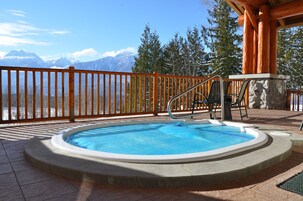 A hot tub with a wooden deck and a view of snow-capped mountains.