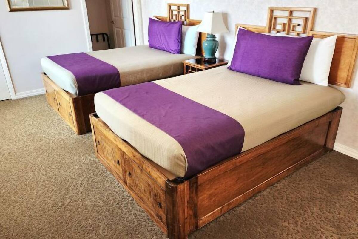Una cama doble con estructura de madera, dos mesitas de noche con lámparas y un edredón morado.