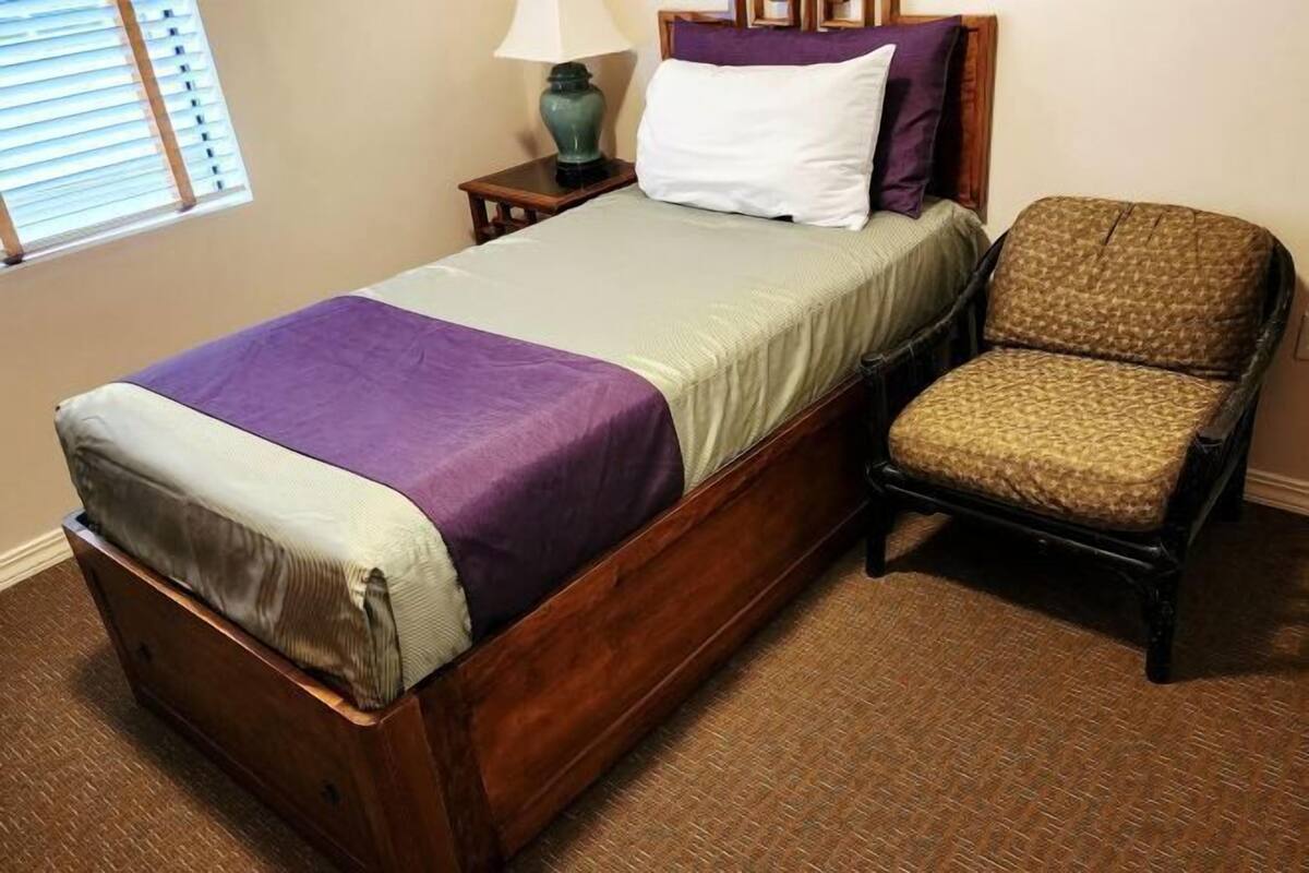 Una cama de madera con cabecera, una silla, una lámpara y una ventana con persianas.