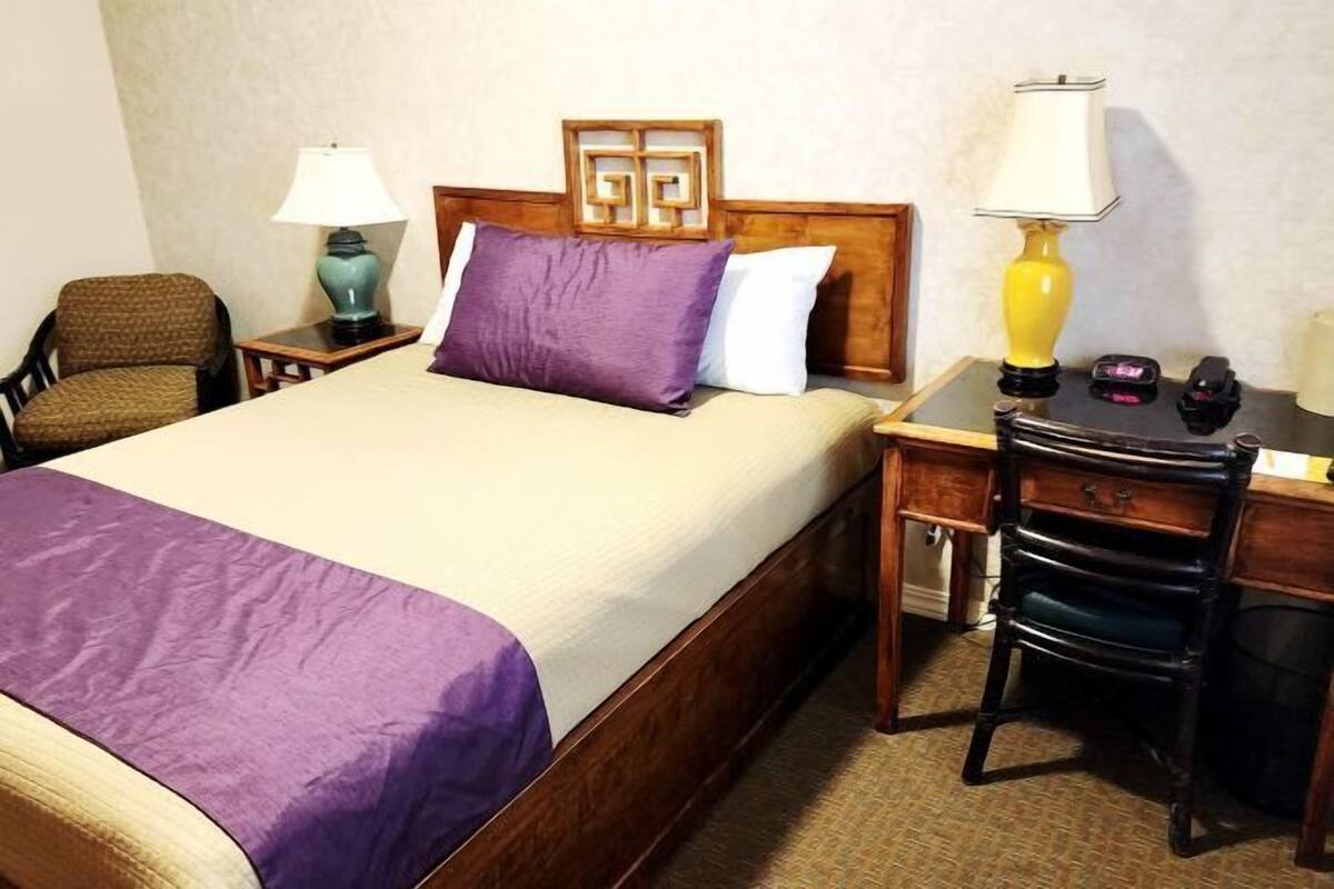Una habitación de hotel con cama, escritorio, silla, lámpara y mesita de noche.