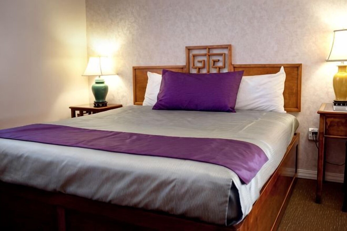 A neatly made bed with a headboard, two bedside lamps, and a wooden nightstand.