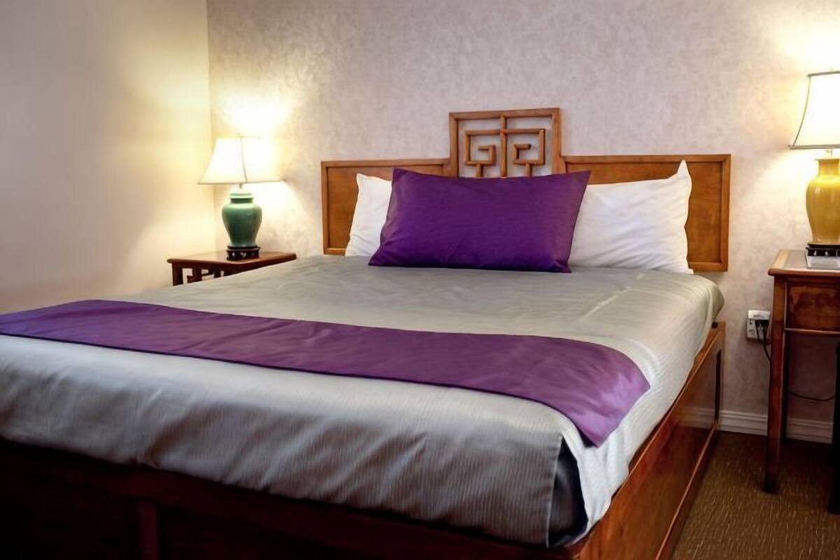 Una cama bien tendida con un cabecero, dos lámparas de noche y una mesita de madera.