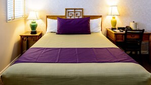 A neatly made bed with a purple pillow and a green blanket, two bedside tables with lamps, a wooden headboard, and a small desk with a chair. - SW Hotel – No Resort Fee (San Francisco)