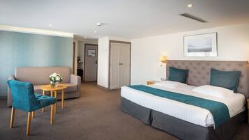A hotel room with a bed, a sofa, a chair, a small table with a vase, and a framed picture on the wall.