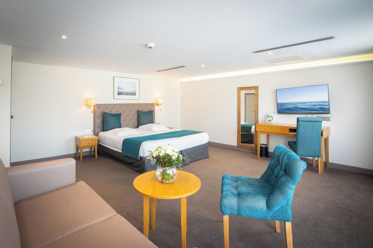 A hotel room with a bed, a desk, a chair, a small table, and a TV.