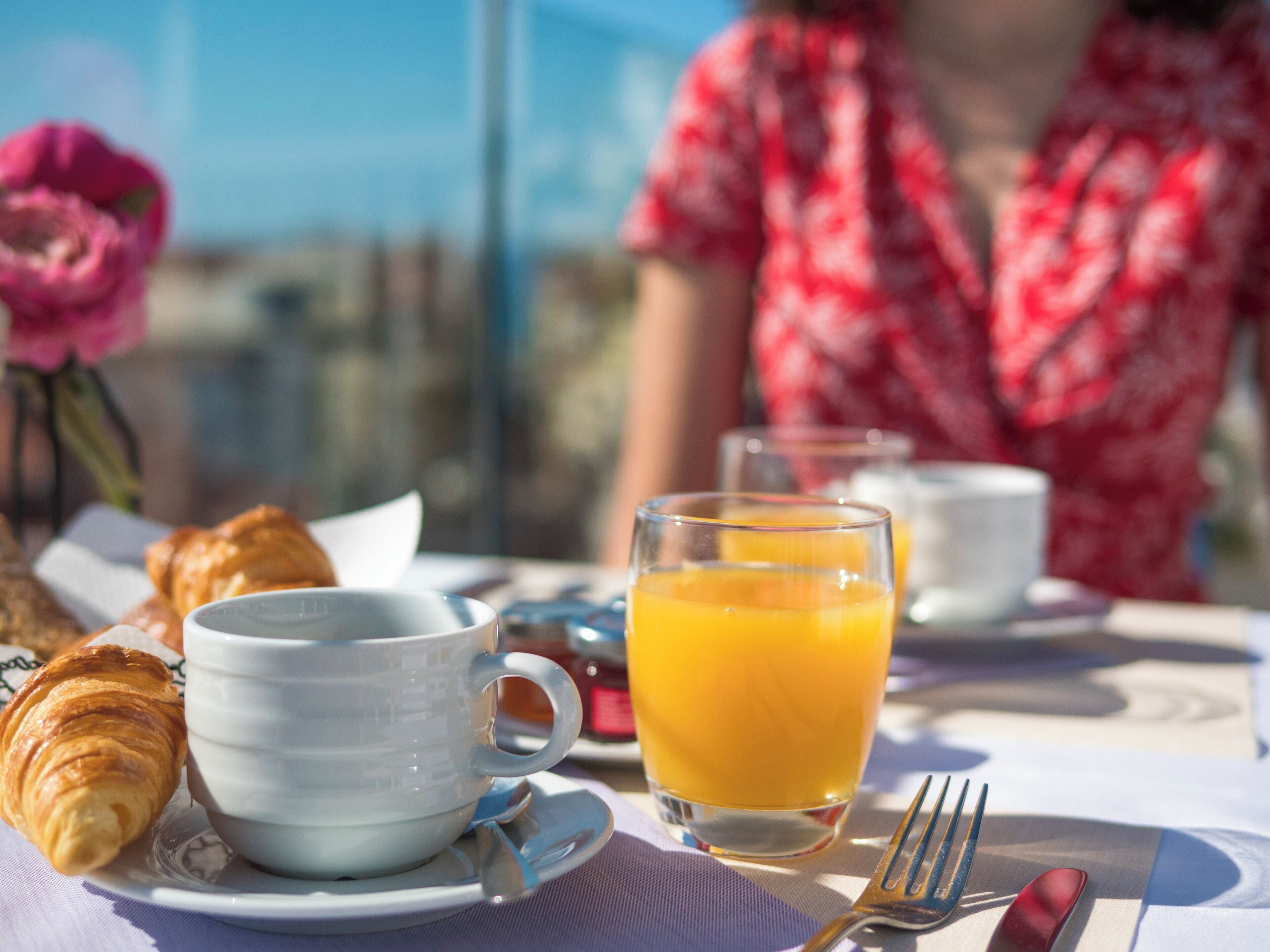 Un desayuno con croissants, una taza, un vaso de zumo de naranja y un tenedor sobre una mesa.