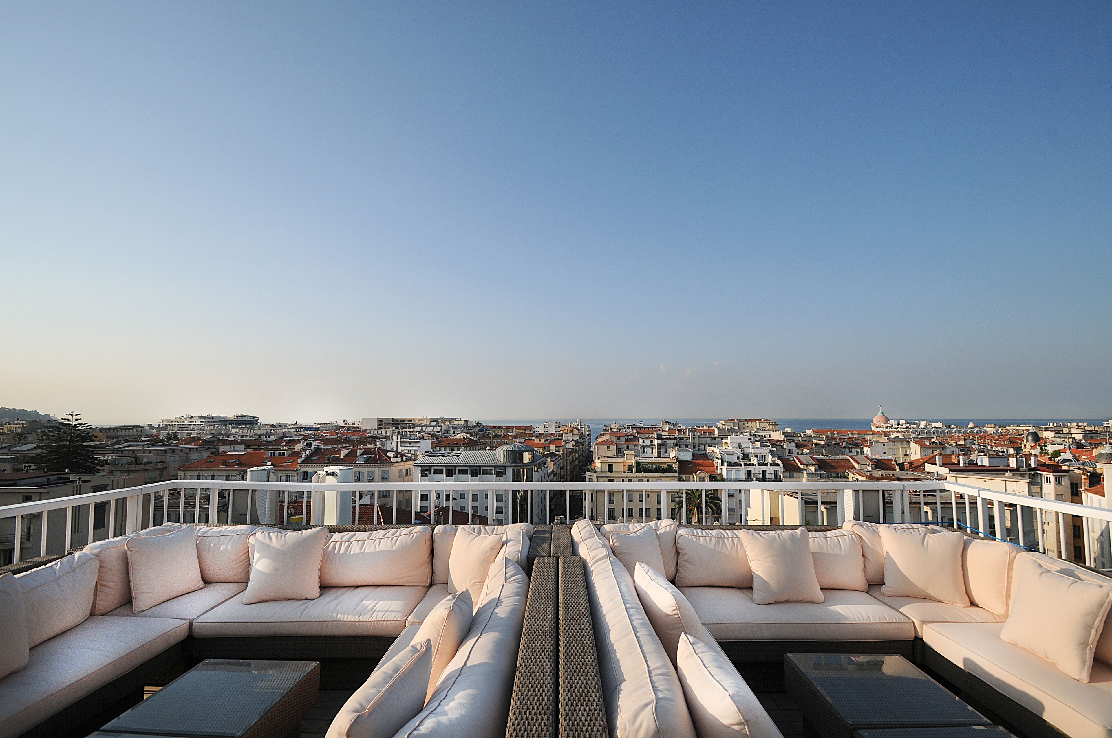 A rooftop terrace with a white cushioned seating area and a view of the cityscape.