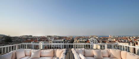 A rooftop terrace with a white cushioned seating area and a view of the cityscape.