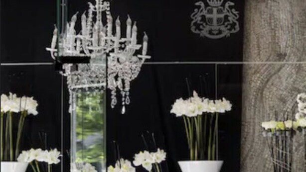 A modern interior with a chandelier, white vases with flowers, and a black wall with a crest emblem. - Splendid Hotel & Spa Nice (Nice)