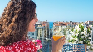A person seated at an outdoor table with a glass of orange juice, a white tablecloth, and a view of a cityscape in the background. - Splendid Hotel & Spa Nice (Nice)