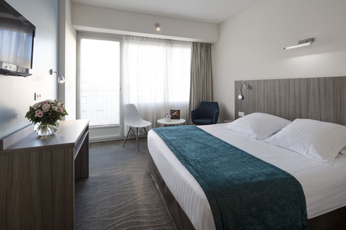 A hotel room with a bed, a desk, a chair, a small table, and a TV.
