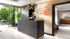 A reception area with a modern design, featuring a reception desk, a large poster on the wall, and a view of the outdoors. - Splendid Hotel & Spa Nice (Nice)