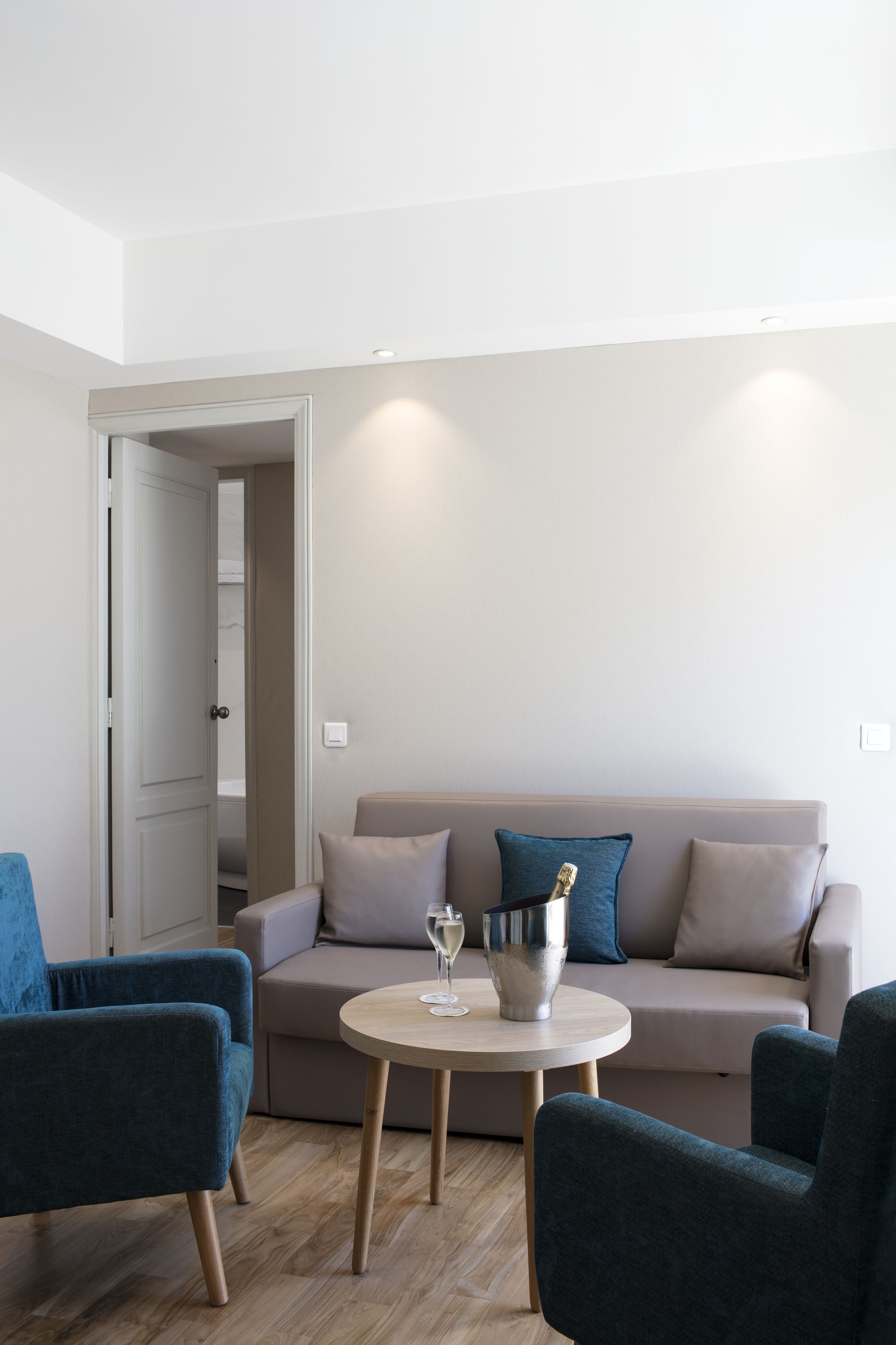 A modern living room with a beige sofa, two blue armchairs, and a round wooden coffee table.