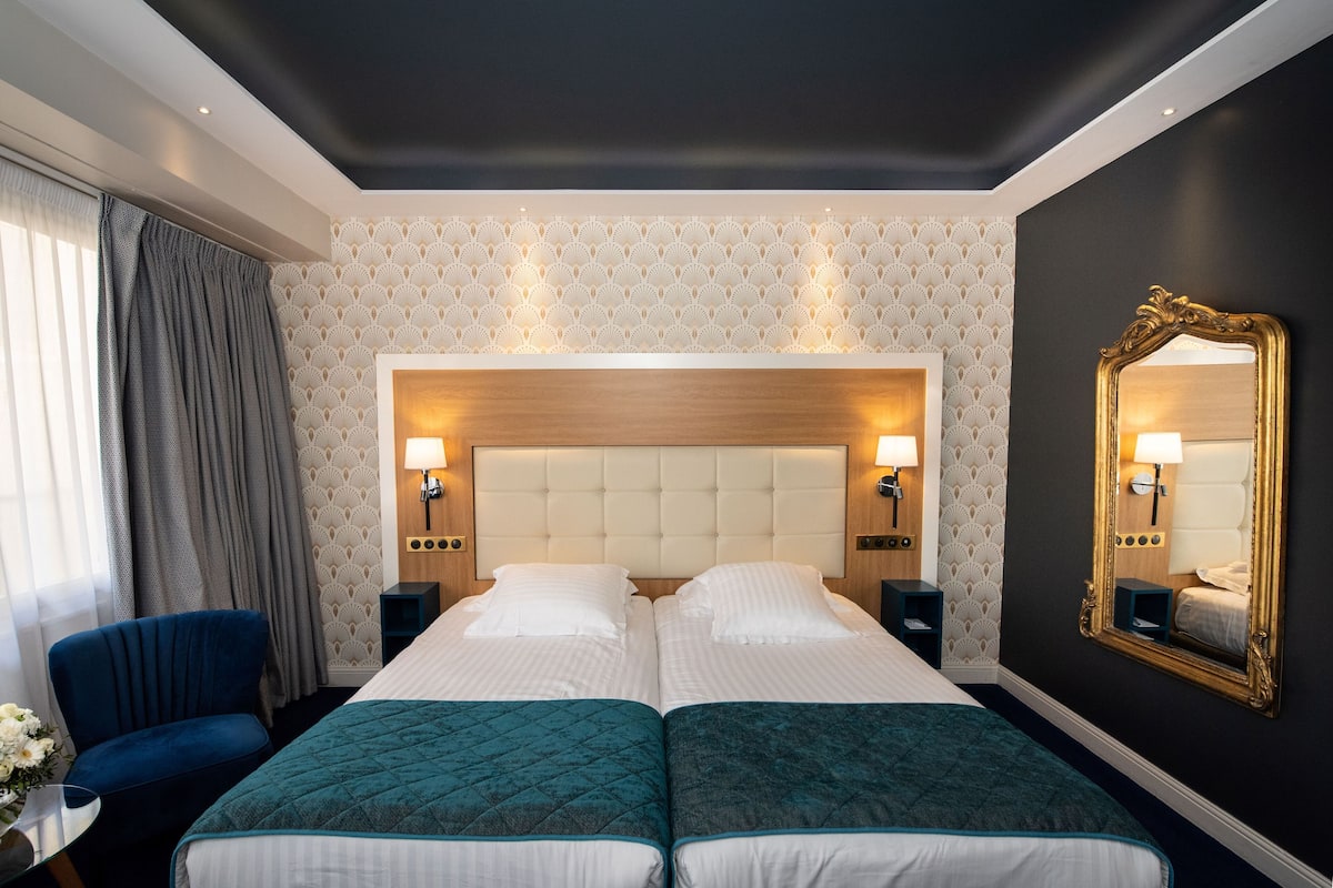 A double bed with a tufted headboard, two bedside tables with lamps, a large mirror, and a blue chair.
