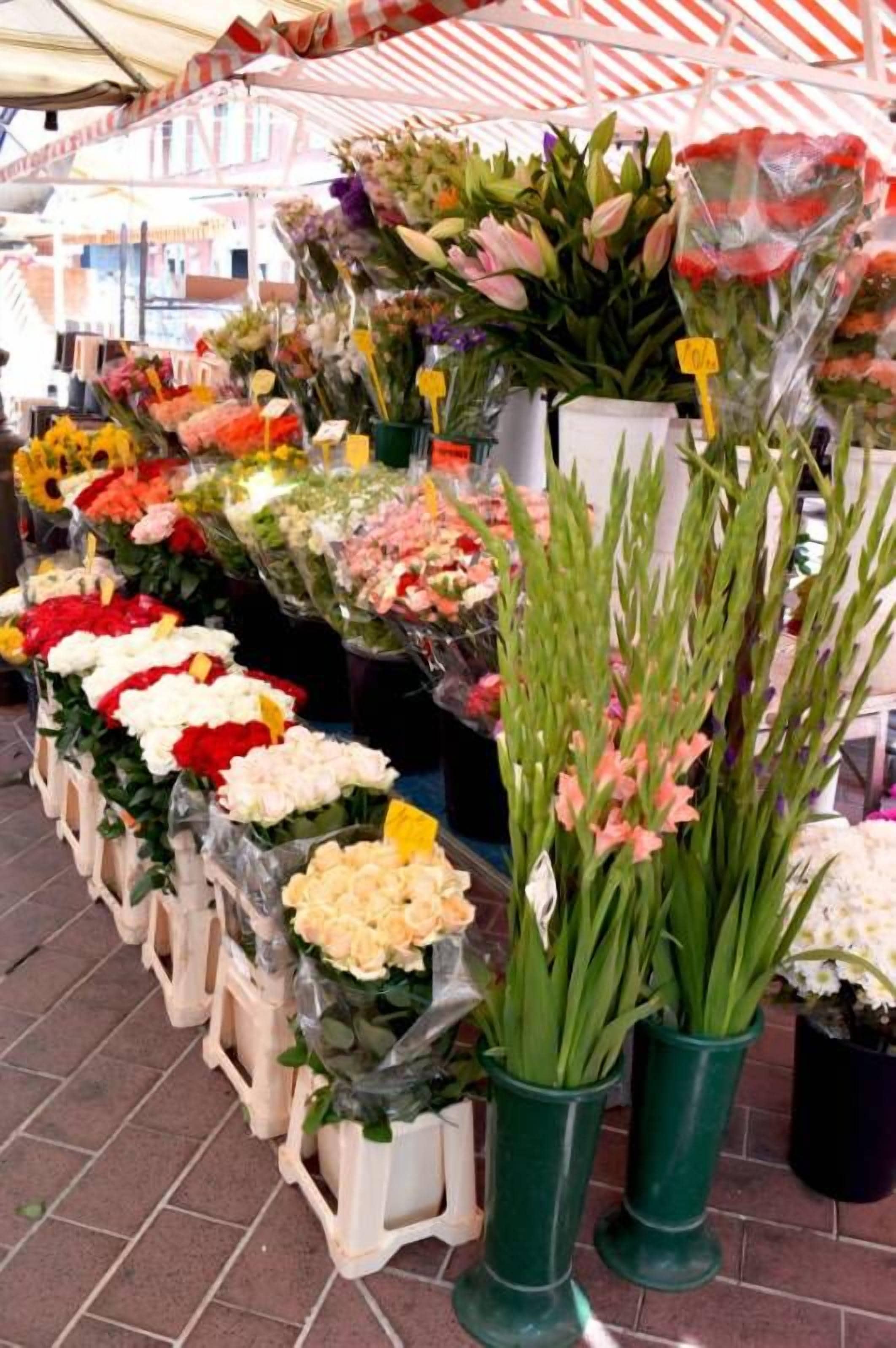 Un aparador de mercat floral amb diverses flors en testos i cistells, sota una tenda de tires.