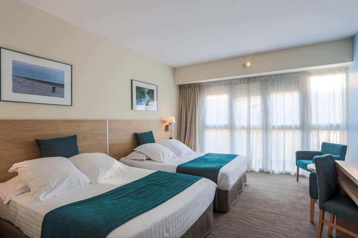 A hotel room with two beds, a desk, and a chair. There are two framed pictures on the wall.