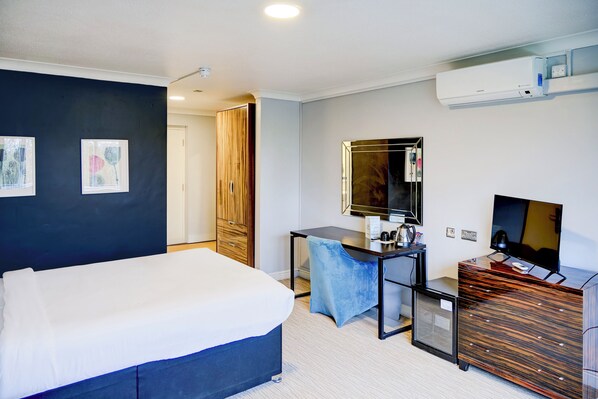 Habitación de hotel con cama, escritorio y silla, cómoda, televisor y espejo.