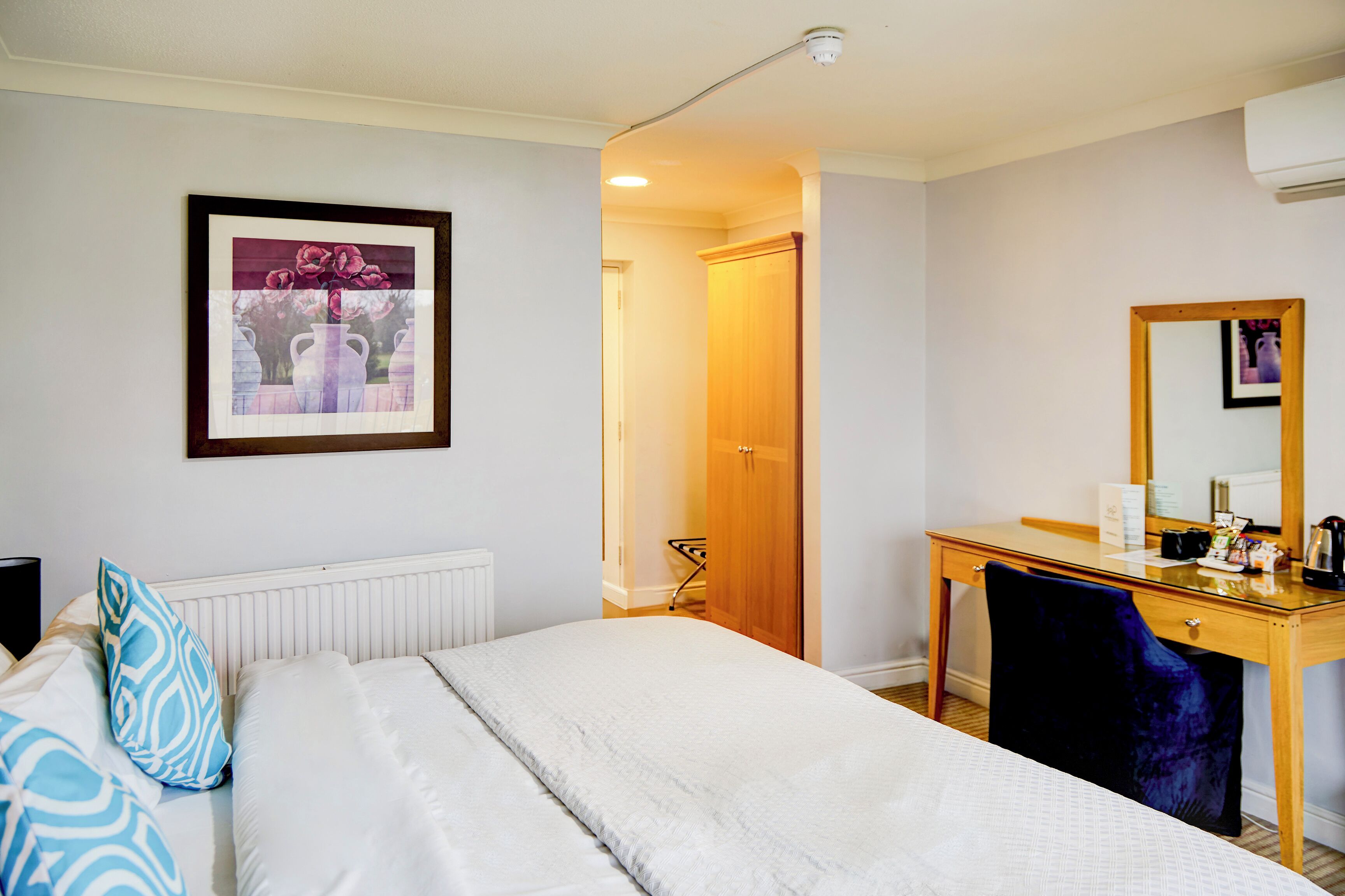 A hotel room with a bed, a desk, a chair, a mirror, and a framed picture on the wall.