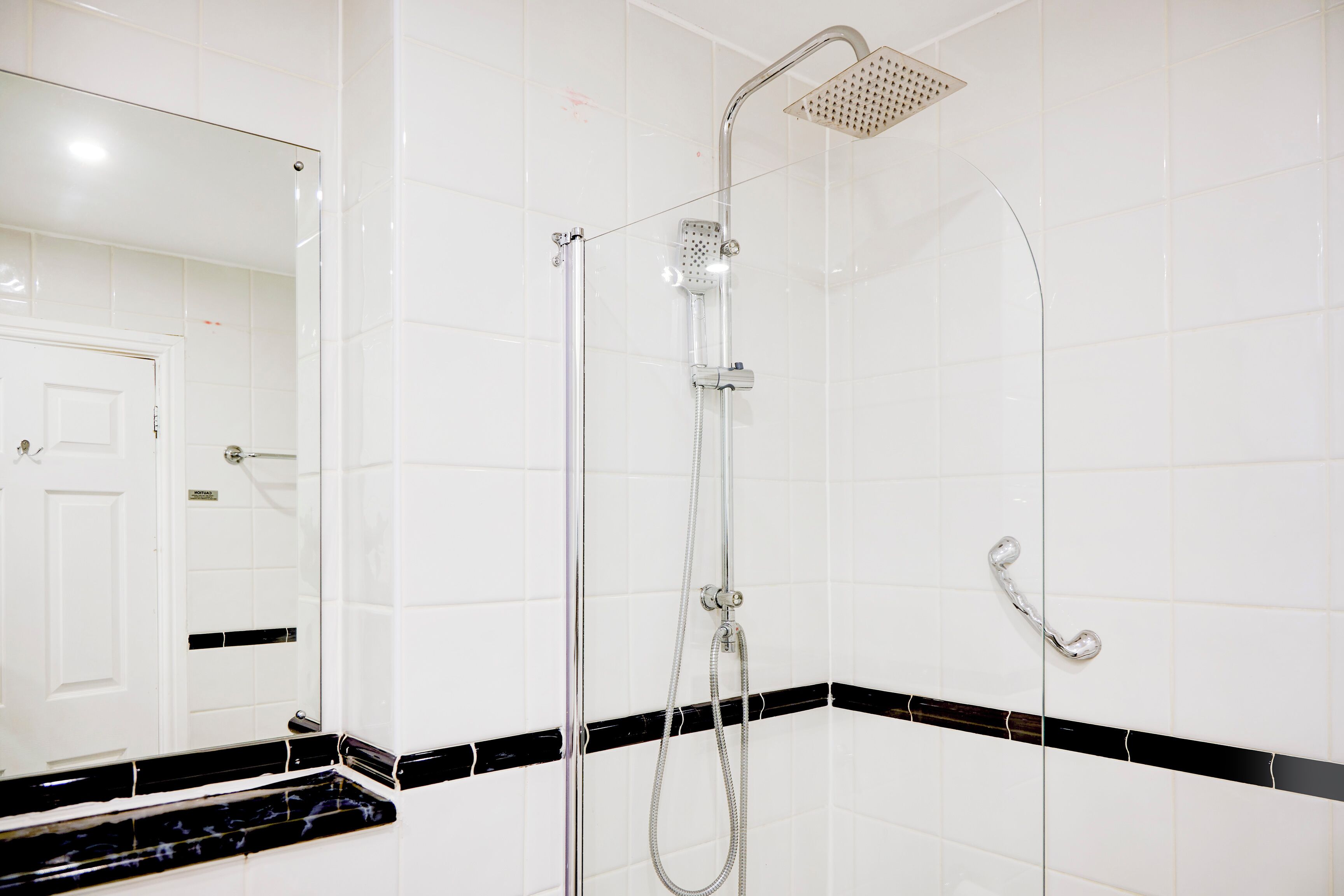 A bathroom with white tiled walls, a black and white marble countertop, a shower with a handheld showerhead, and a glass-enclosed shower area.