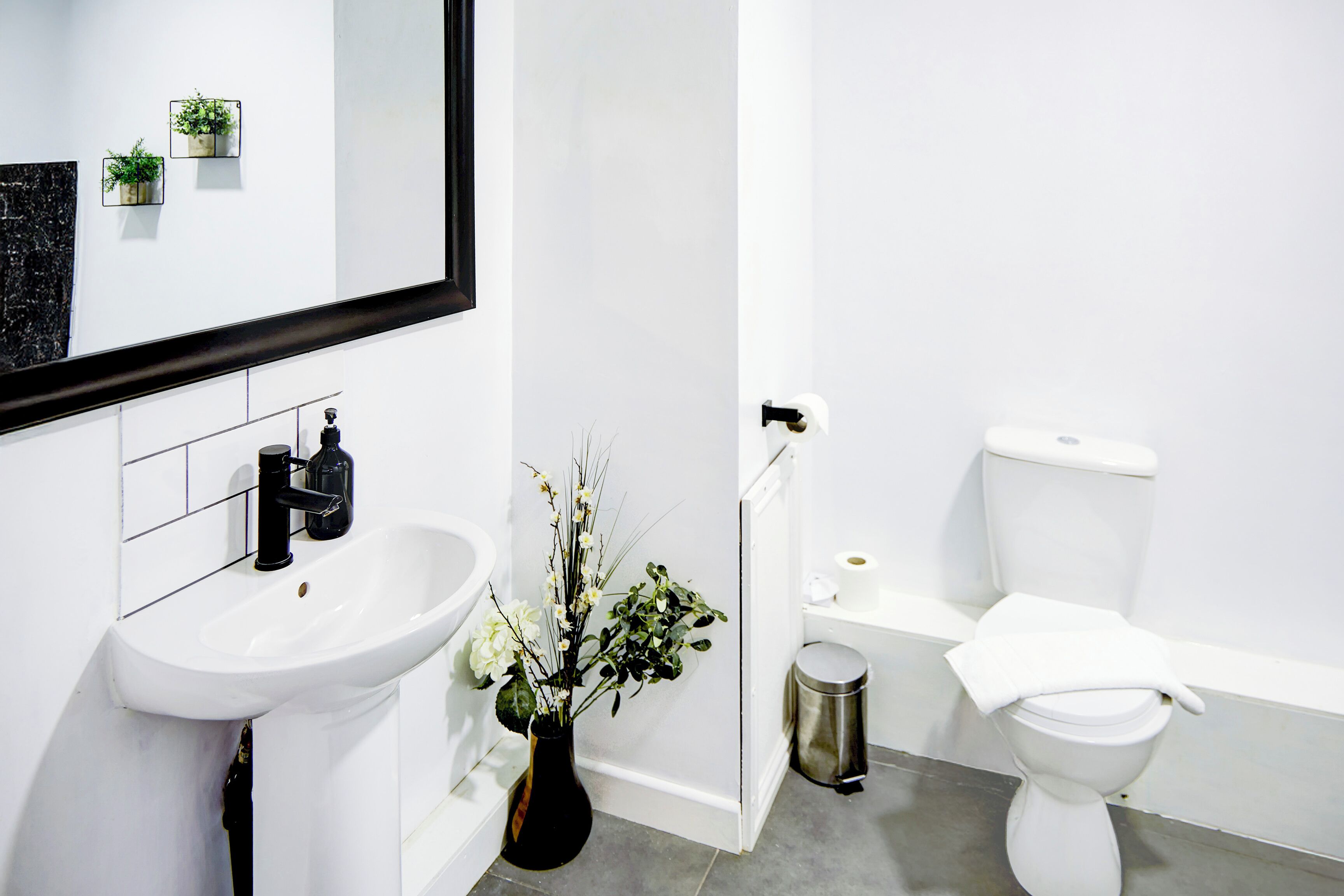 A modern bathroom with a white sink, a mirror, a toilet, and a trash can.