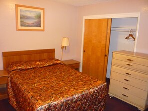 A bedroom with a bed, a dresser, a lamp, and a door. - Nice Inn Yuba City (Yuba City)
