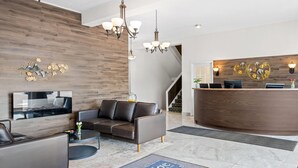 A modern hotel lobby with a reception desk, leather sofas, a flat-screen TV, and a decorative wall piece.